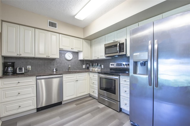 kitchen with sink, appliances with stainless steel finishes, tasteful backsplash, light hardwood / wood-style flooring, and white cabinets