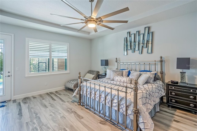 bedroom with a raised ceiling, light wood-type flooring, access to outside, and ceiling fan