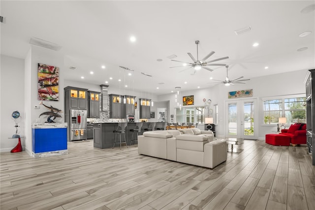 living area featuring visible vents, baseboards, french doors, light wood-type flooring, and recessed lighting