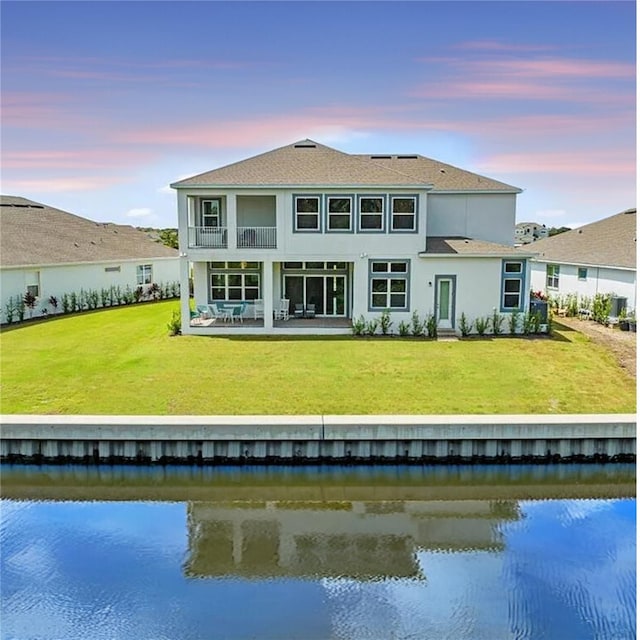 back house at dusk with a lawn and a water view