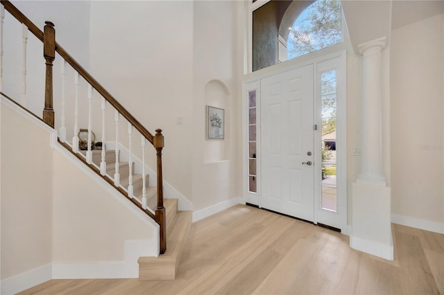 foyer entrance with light wood-type flooring, decorative columns, and a towering ceiling