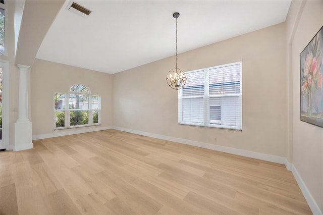 empty room with light wood-type flooring, a chandelier, and decorative columns