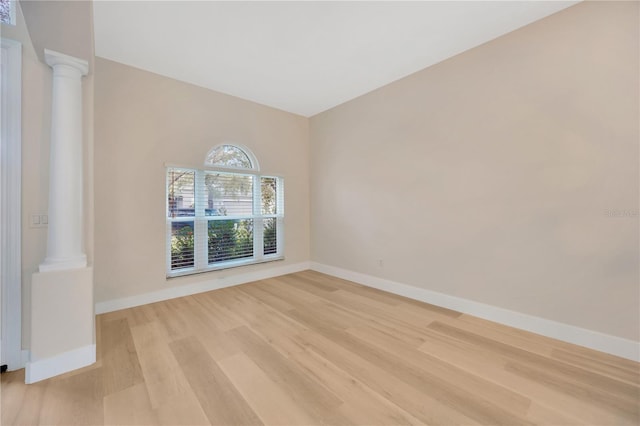 unfurnished room featuring ornate columns and light wood-type flooring