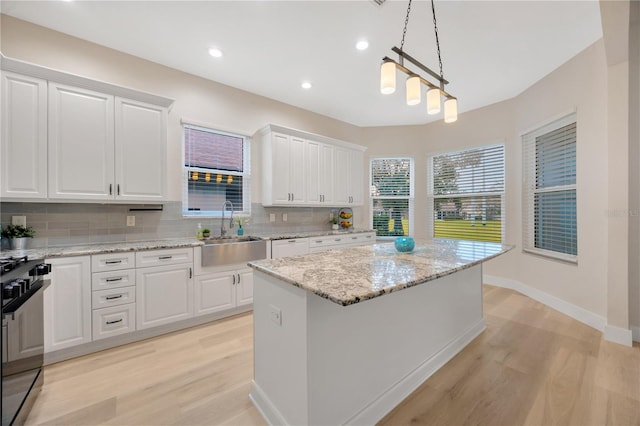 kitchen with white cabinetry, a sink, light wood-style floors, range with gas cooktop, and tasteful backsplash