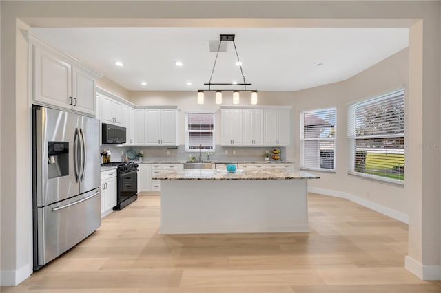 kitchen with a center island, white cabinets, light stone counters, and stainless steel appliances