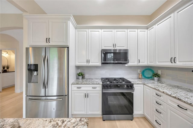 kitchen with light hardwood / wood-style flooring, appliances with stainless steel finishes, decorative backsplash, and white cabinets