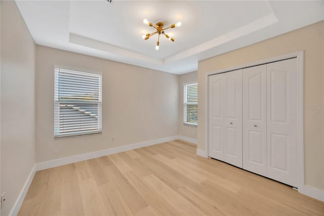 unfurnished bedroom featuring multiple windows, a tray ceiling, and a closet