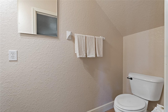 bathroom featuring lofted ceiling, baseboards, toilet, and a textured wall