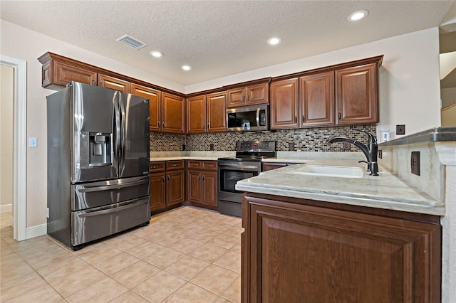 kitchen featuring light tile patterned floors, a peninsula, a sink, appliances with stainless steel finishes, and backsplash