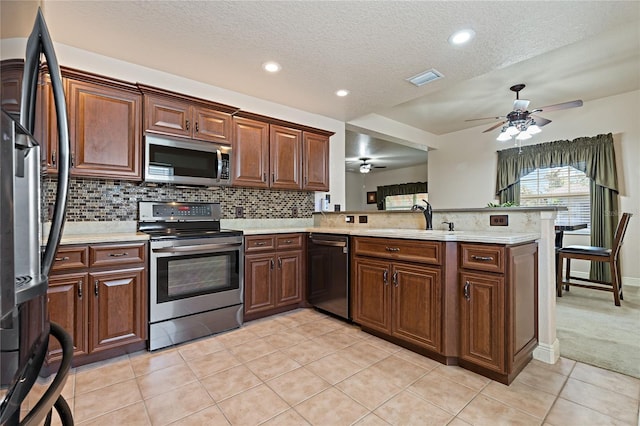 kitchen featuring stainless steel appliances, light countertops, backsplash, a sink, and a peninsula