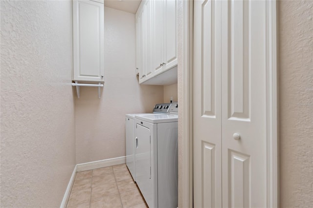 clothes washing area featuring light tile patterned floors, cabinet space, a textured wall, independent washer and dryer, and baseboards