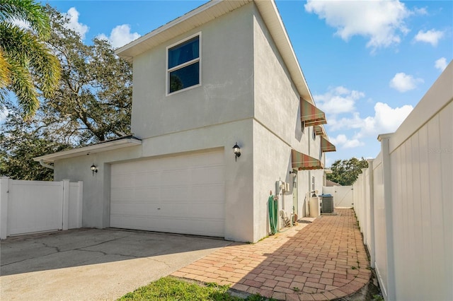 view of side of property with stucco siding, fence, a gate, and central air condition unit