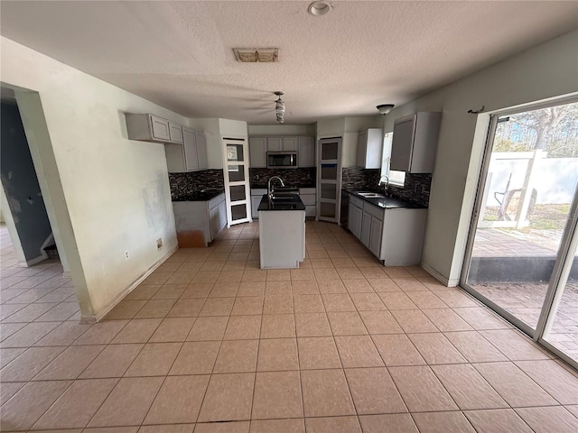 kitchen with stainless steel appliances, sink, light tile patterned floors, an island with sink, and gray cabinetry