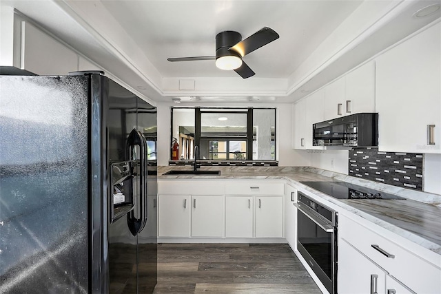 kitchen with a tray ceiling, dark wood-type flooring, sink, black appliances, and white cabinetry