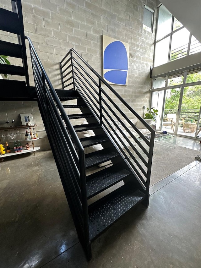 stairs with concrete block wall, concrete floors, and a high ceiling