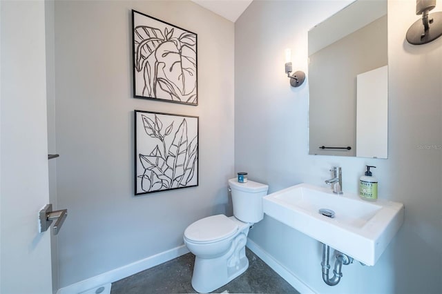 half bath with toilet, baseboards, and a sink