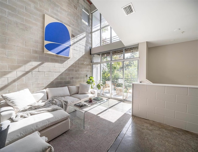 living area with a healthy amount of sunlight, visible vents, concrete floors, and a high ceiling