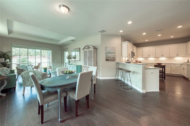 dining space featuring dark hardwood / wood-style flooring, a textured ceiling, and a tray ceiling