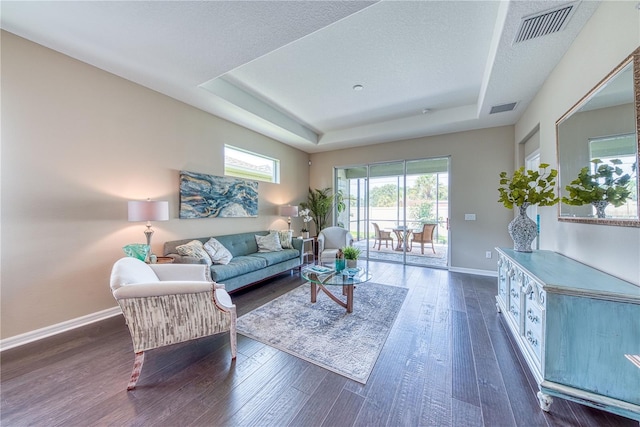 living room with a textured ceiling, dark hardwood / wood-style floors, and a tray ceiling