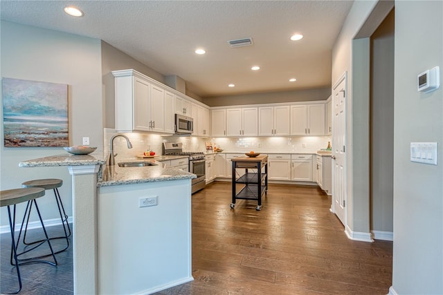 kitchen with stainless steel appliances, white cabinetry, dark hardwood / wood-style flooring, sink, and kitchen peninsula