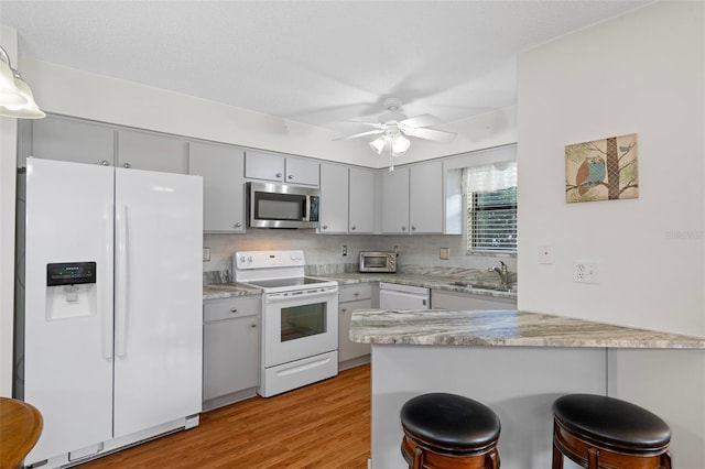 kitchen featuring light wood-type flooring, white appliances, a kitchen breakfast bar, kitchen peninsula, and ceiling fan