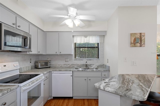 kitchen featuring white appliances, sink, kitchen peninsula, ceiling fan, and light hardwood / wood-style flooring