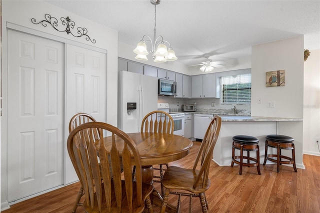 dining room with light wood-type flooring, ceiling fan with notable chandelier, and sink