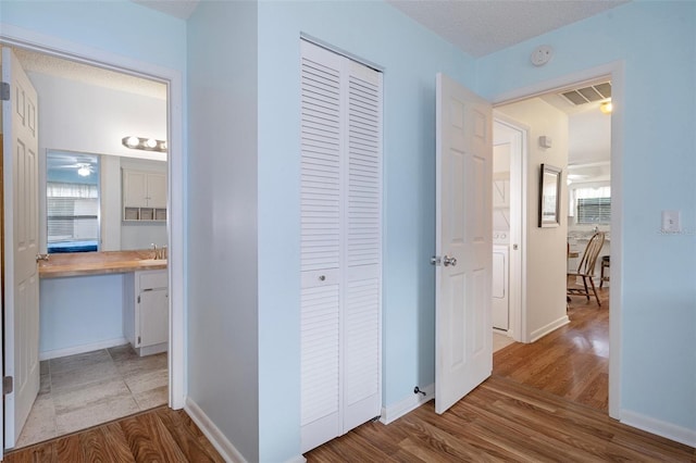 hall with sink, light wood-type flooring, and a textured ceiling