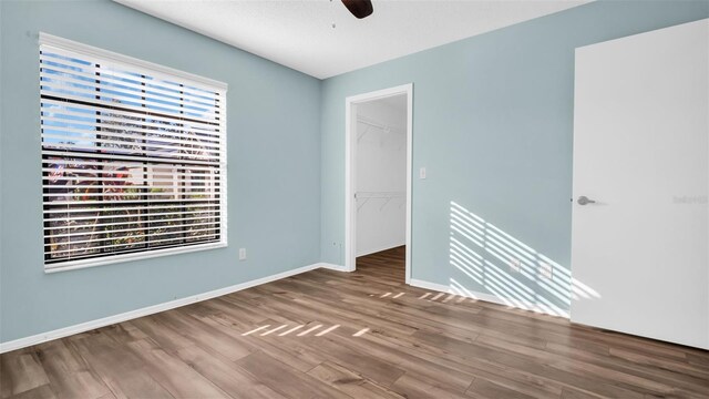 3499 Cedar Ln, Palm Harbor, FL 34684 - unfurnished bedroom featuring wood finished floors, a walk in closet, a closet, baseboards, and a ceiling fan