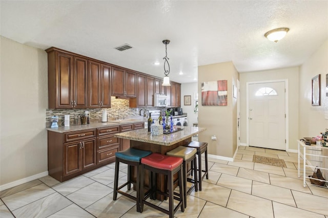 kitchen featuring sink, hanging light fixtures, tasteful backsplash, a kitchen island, and a kitchen bar