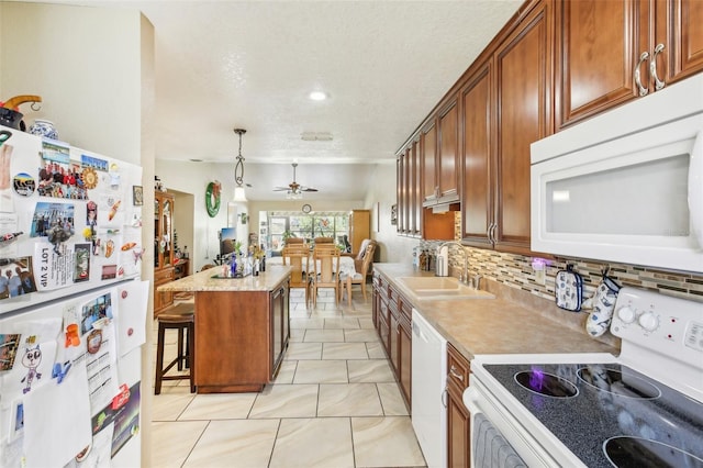 kitchen with a kitchen bar, a textured ceiling, white appliances, a kitchen island, and hanging light fixtures