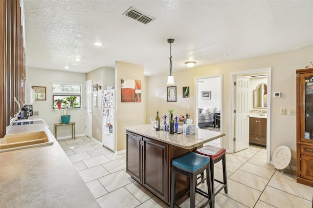 kitchen featuring a kitchen bar, sink, light tile patterned floors, decorative light fixtures, and a kitchen island