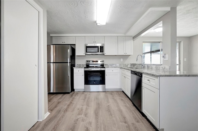 kitchen with stainless steel appliances, light hardwood / wood-style floors, sink, a textured ceiling, and white cabinets