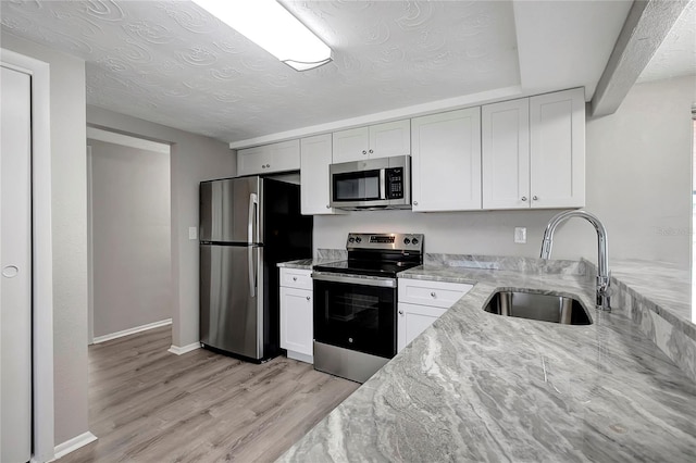 kitchen featuring stainless steel appliances, light stone countertops, white cabinetry, and light hardwood / wood-style flooring