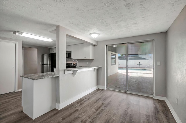 kitchen featuring wood-type flooring, stainless steel appliances, a textured ceiling, white cabinets, and kitchen peninsula