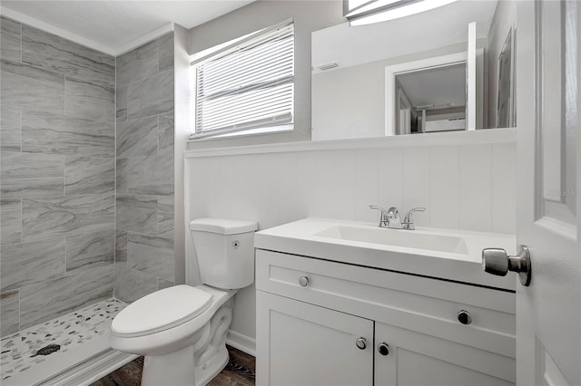 bathroom with hardwood / wood-style floors, vanity, toilet, and a tile shower