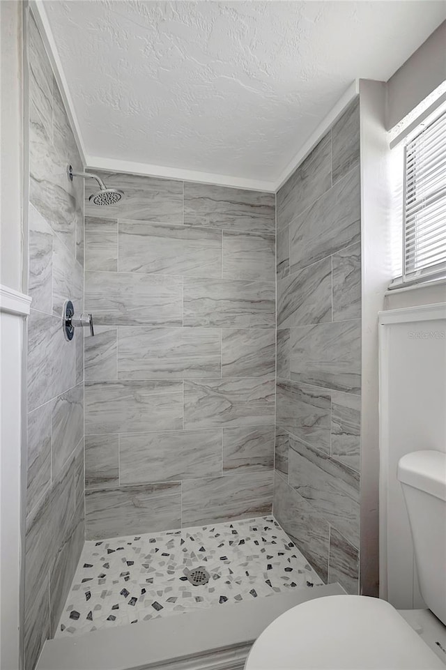 bathroom featuring a textured ceiling, toilet, and a tile shower