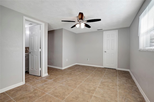 empty room with a textured ceiling, ceiling fan, and light tile patterned floors