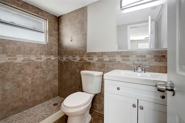 bathroom with vanity, toilet, a tile shower, and tile walls