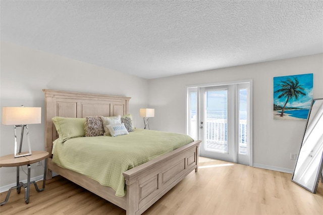 bedroom with access to exterior, light hardwood / wood-style floors, and a textured ceiling