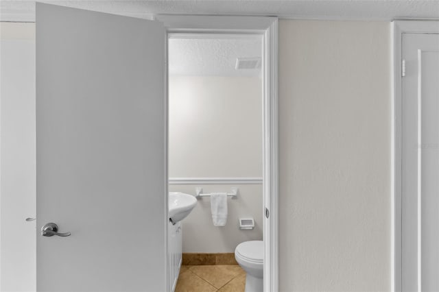 bathroom with a textured ceiling, toilet, and tile patterned floors