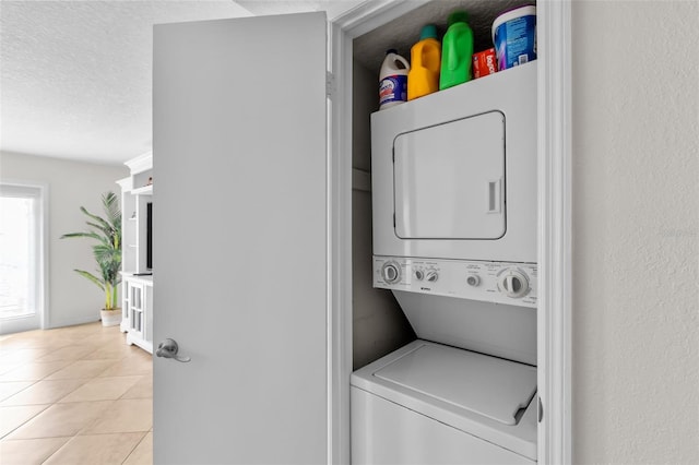 clothes washing area featuring a textured ceiling, stacked washer and clothes dryer, and light tile patterned flooring