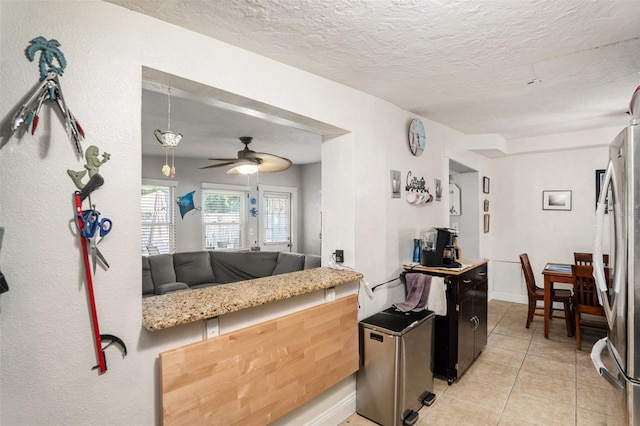 kitchen featuring kitchen peninsula, a textured ceiling, light tile patterned floors, ceiling fan, and stainless steel refrigerator