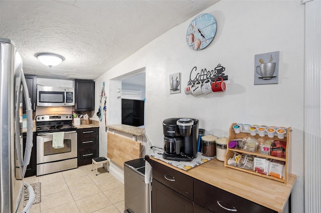 kitchen with a textured ceiling, light tile patterned flooring, and stainless steel appliances