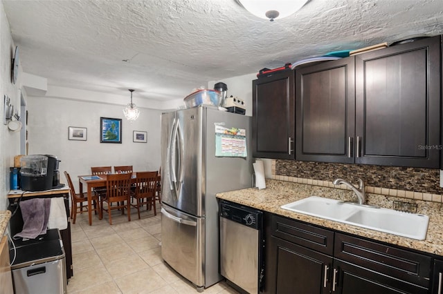 kitchen with stainless steel appliances, a textured ceiling, sink, light stone countertops, and decorative light fixtures