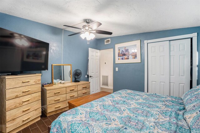 bedroom with a textured ceiling, dark wood-type flooring, ceiling fan, and a closet