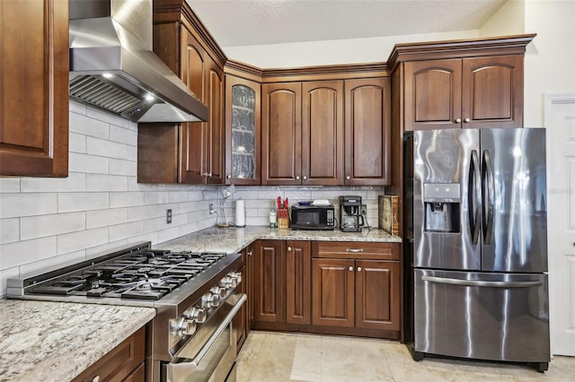 kitchen with backsplash, light stone countertops, wall chimney range hood, and stainless steel appliances