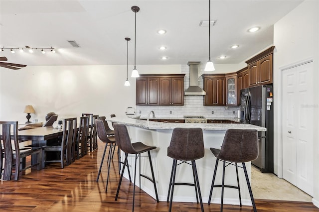 kitchen featuring black fridge, wall chimney exhaust hood, a large island, and dark hardwood / wood-style floors