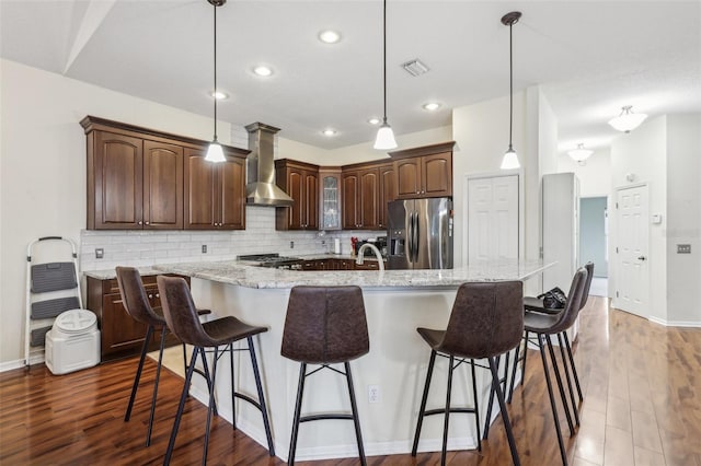 kitchen with a large island, dark hardwood / wood-style flooring, wall chimney range hood, and appliances with stainless steel finishes