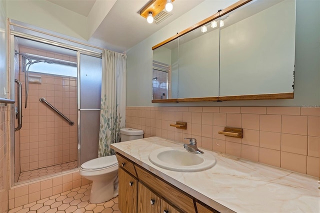 bathroom with vanity, toilet, tile walls, tile patterned flooring, and a tile shower